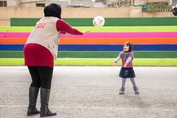 Mercy corps employee and student toss a ball back and forth.