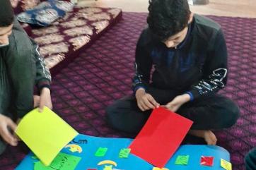 Refugee children sitting on rug working on poster.