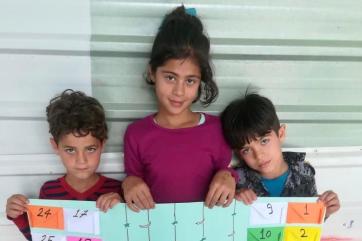 Three refugee children holding a poster.