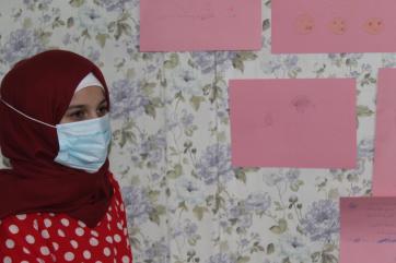 A young person stands next to a wall with artwork.