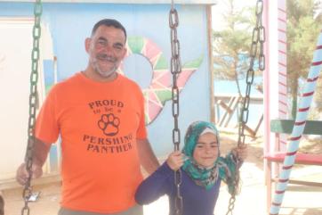 An adult pushing a child on a swing.