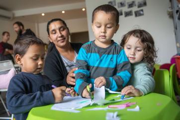 A parent watches children crafting at a small table. 