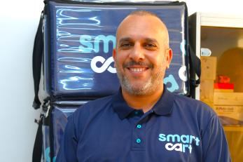 Smart cart owner, smiling, in front of merchandise.