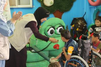 A young person shakes the hand of a frog sculpture.