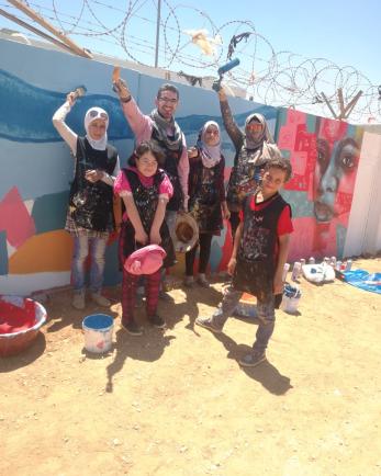 A group of young people and their instructor celebrate their work by a mural they painted.