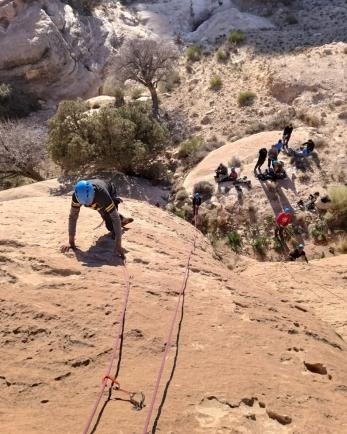 A young person uses climbing ropes to scale the side of a rock face.