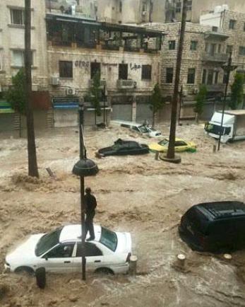 An amman resident stands on top of his car as floodwaters surround other vehicles in the neighborhood.