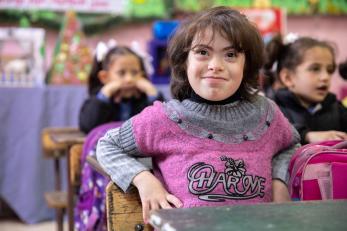 Young Jordanian special needs student sits and smiles in classroom.