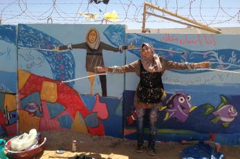 A young person poses in front of a mural of herself.