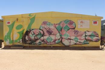 Graffiti of a young girl sleeping in joy and peace on the side of a building in Za'atari Camp, Jordan.