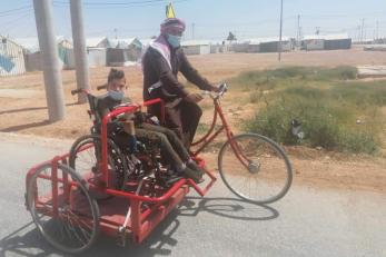 An adult rides a bicycle with a side trolly to transport a wheel chair bound person.