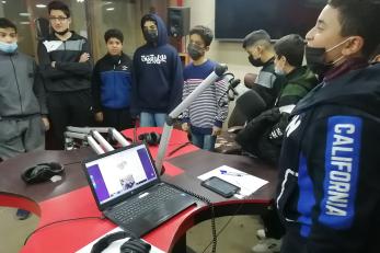 A group of young people cluster around a table with audio recording equipment.
