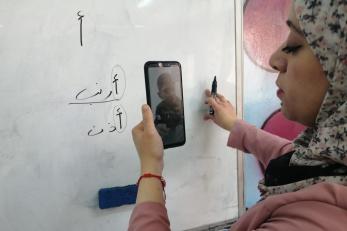 An adult writes on a dry-erase board while video chatting with a youth.