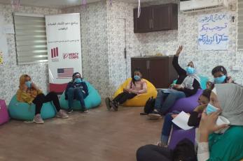 Young people listen to a presentation while sitting on bean bag chairs.