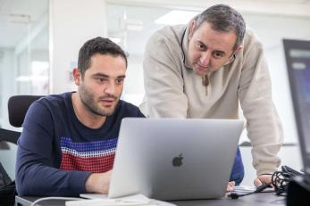 An adult uses a laptop while another looks on.