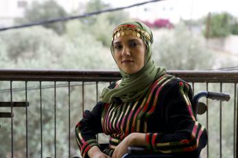 Jordanian woman sitting on a porch with trees in the background.