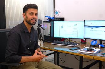 Jordanian business owner sits at computer station smiling.