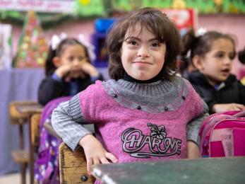 Young jordanian special needs student sits and smiles in classroom.