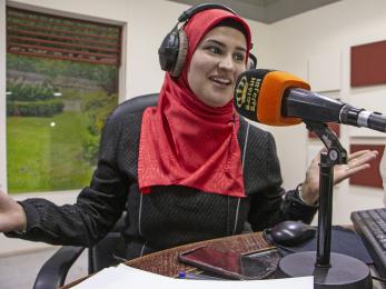 A person wearing headphones speaks into a microphone inside a broadcast studio in jordan. 