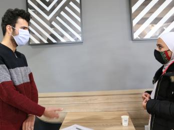 Two people wearing face masks look at each other and have a conversation.