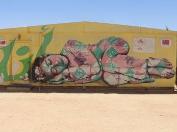 Graffiti of a young girl sleeping in joy and peace on the side of a building in za'atari camp, jordan.