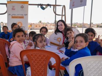 Children sitting around a table, smiling at the camera, while making art.