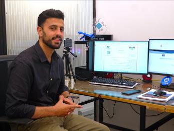 Jordanian business owner sits at computer station smiling.